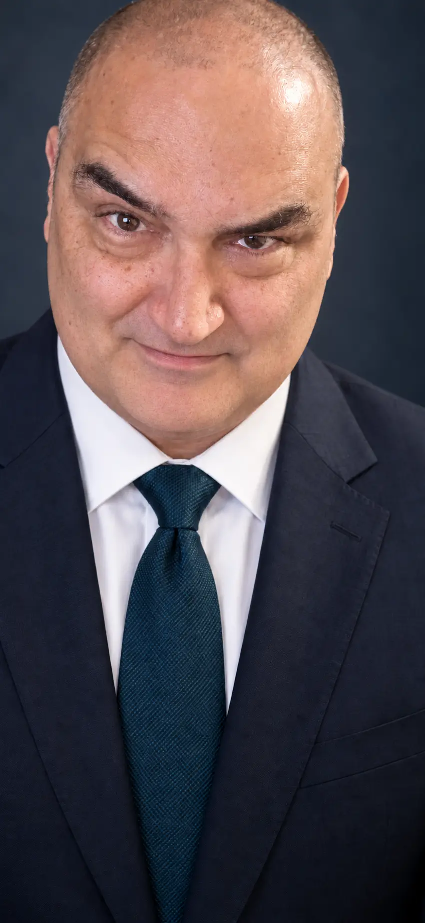 Polished corporate portrait of Tunc Olcer in a navy suit